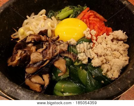 Classic Korea food vegetable Bibimbap hot stone potrice carrotspinachmushroomcucumberseaweedraw yolk egghot spicy chili saucefocus-on-foreground blur backgroundAsian meal close up