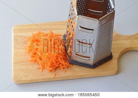 Step by step cooking. Grated carrots with a grater on a wooden cutting board on a grey background