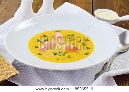 Pumpkin puree soup with prawns in a white plate on a wooden background. Healthy eating concept