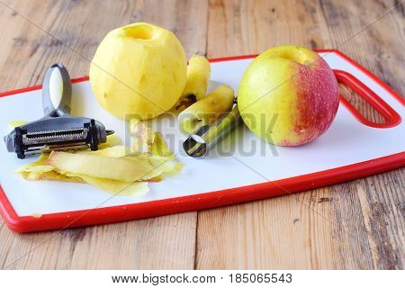 Pealed apples wih the core taken away with special knives on a white cutting board on a wooden background. Step by step cooking. Healthy eating concept