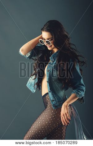 gorgeous girl in a fashionable white sunglasses, dressed in a blue jeance jacket and transparent tights without panties. posing standing near stylish transparent armchair. side view, waist portrait