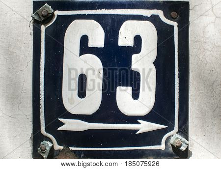 Weathered grunge square metal enameled plate of number of street address with number 63 closeup