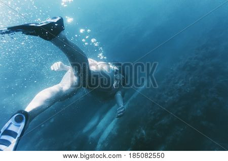 Young woman free diver in flippers with mask and snorkel swimming underwater to seaweed rear view.