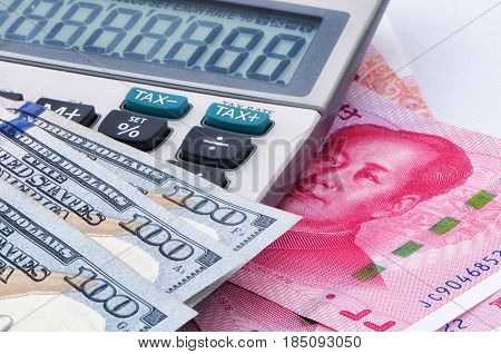 Chinese 100 Renminbi and 100 U.S. dollar bills piled on a white background.