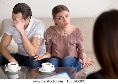 Portrait of unhappy couple consulting marriage counselor or family psychologist. Young emotional woman telling specialist about problems, her husband sitting next to wife frustrated and depressed