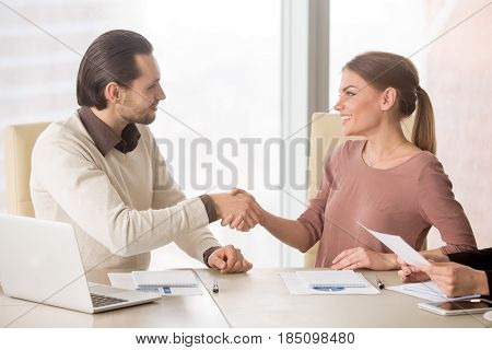 Smiling businesswoman handshaking with young male colleague, introducing herself before office meeting discussion, starting teamwork on project, new members of team shaking hands getting acquainted