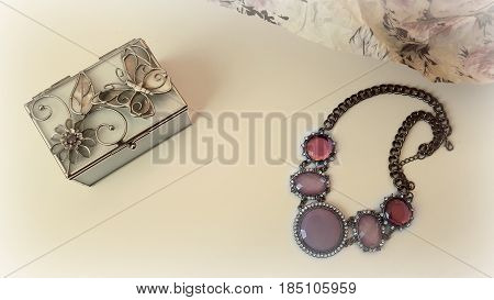 Jewelry box and necklace with purple rhinestones on a white table. Filter patina.