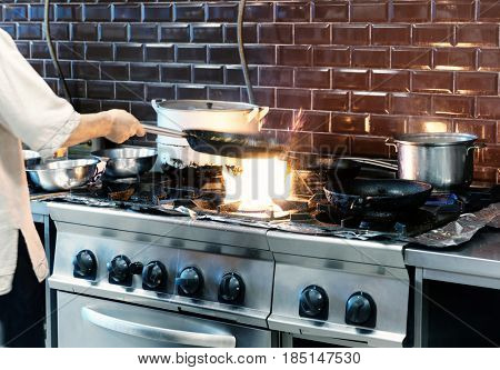 Chef is making flambe dish in restaurant kitchen, motion blur, toned image