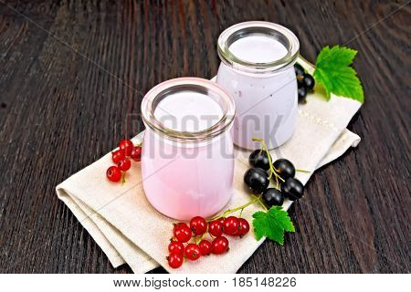 Milkshake with red and black currants in glass jars on a napkin with berries on a background of a dark wooden board
