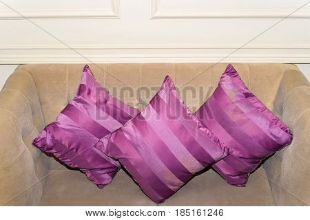 Close up of three purple cushions lying on white sofa