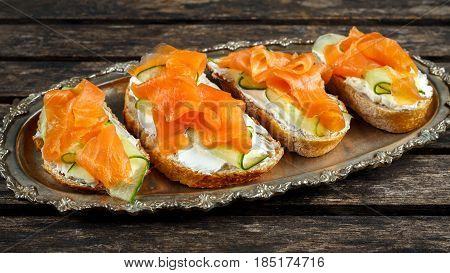 Smoked salmon bruschettas with soft cheese and cucumber shavings on a vitage plate.