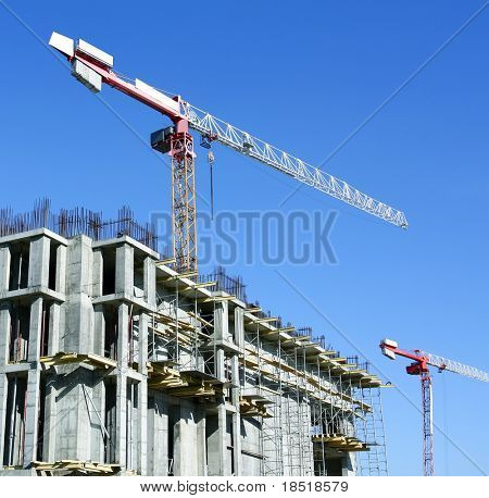 two moving yellow cranes over unfinished house