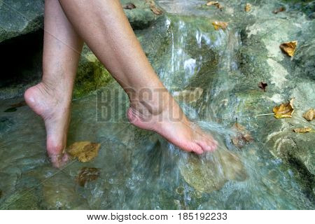 Beautiful female legs in the running cool water of a mountain stream. Beauty and health.