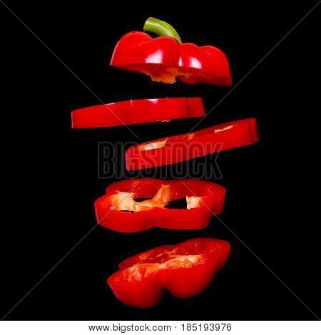 Flying red paprika. Sliced floating pepper isolated. Levity capsicum vegetable isolated on black background