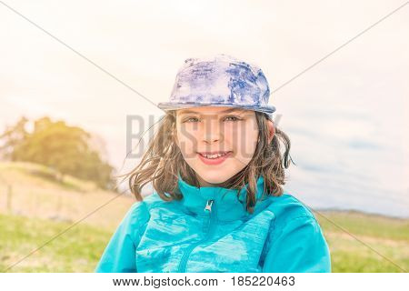 Outdoor portrait of cute young girl in blue jacket and cap with wind in her hair.