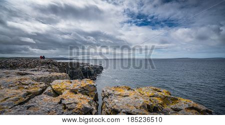 Two unidentified people sitting on the cliffs edge in Doolins Bay, The Burren, County Clare, Ireland