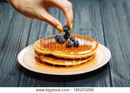 Chef garnishing a stack of pancakes with golden honey and fresh blueberries, close up of his hand and the blueberries