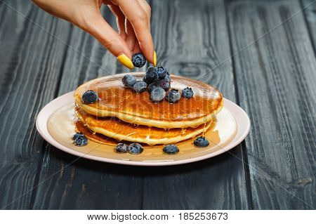 Chef garnishing a stack of pancakes with golden honey and fresh blueberries, close up of his hand and the blueberries