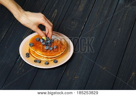 Chef garnishing a stack of pancakes with golden honey and fresh blueberries, close up of his hand and the blueberries
