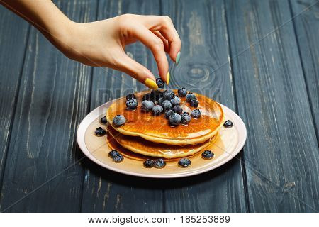 Chef garnishing a stack of pancakes with golden honey and fresh blueberries, close up of his hand and the blueberries