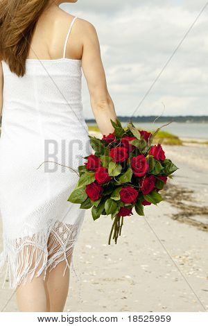 ダースのバラとビーチを歩いて白いドレスを着た女性