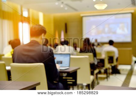Blurred Image Of Education People, Business People And Students Sitting In Large Hal With Screen And