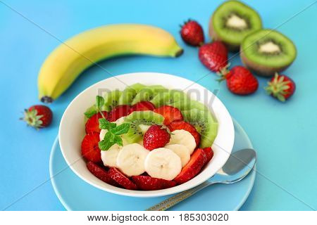 Fruit salad of kiwi, strawberry and banana and ingredients on a blue background. Horizontal.