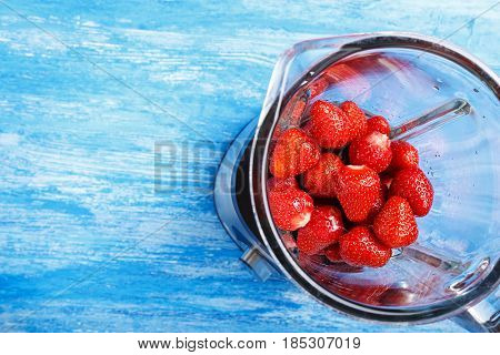 peeled ripe strawberries in a blender on a blue wooden table