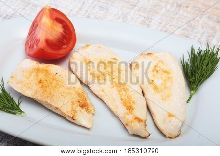 Slices of roasted chicken breast and tomato on white plate.