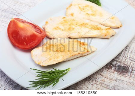 Slices of roasted chicken breast and tomato on white plate.