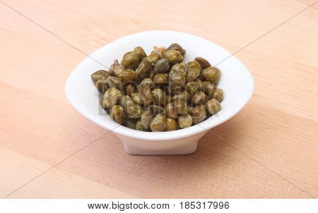 bowl with fresh capers on wooden table.