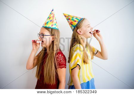 Two girls blowing birthday pipes on a white background