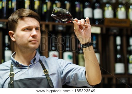 Bokal of red wine on background of male sommelier appreciating color, quality, flavor and sediments of drink. Professional degustation expert in winemaking.