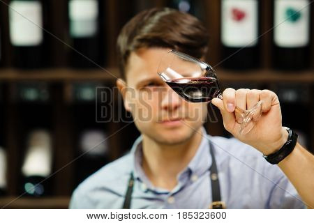 Bokal of red wine on background of male sommelier appreciating color, quality, flavor and sediments of drink. Professional degustation expert in winemaking.