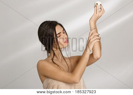 Woman in bath towel  applying moisturizer on left hand after bathing. Sking and beauty care.