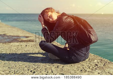 beautiful woman in jeans and jacket sitting on the breackwater.