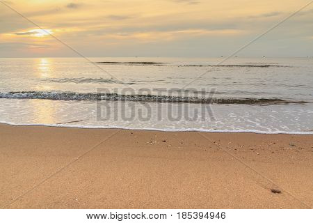 Soft wave of sea on sandy beach with sunrise in morning