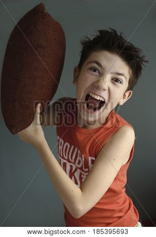 teenager mischivous boy fighting with pillow open mouth close up portrait