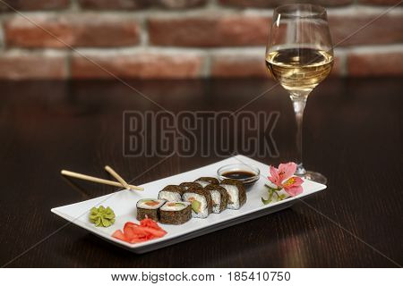 Philadelphia maki sushi rolls with salmon cheese cream cucumber on white plate and glass of wine