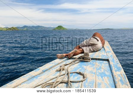 Indonesian sailor resting on the bow of his ship in transit to islands Komodo