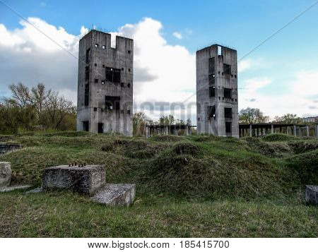Two half-ruined towers in the wasteland. Two Unfinished high-rise buildings against the blue sky on a cloudy day