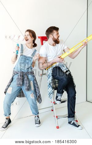Full length portrait of a happy joyful couple holding work tools and having fun while having a break in repairing their house
