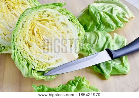 section of young fresh gren head of cabbage cutted with knife against wooden background