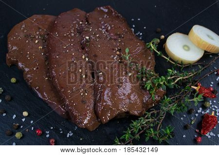 Raw beef liver slice in pieces on slate board with herbs and spices