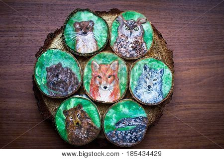 Collection of painted forest animals on a cut pieces of wood. Beautiful natural paint colors. Background of brown wooden cut tree trunk. Red fox grey wolf snake owl bear weasel and beaver. Wild nature