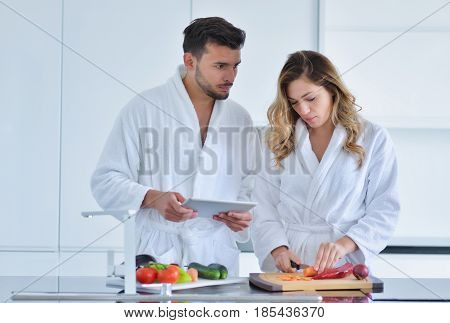 Couple in home kitchen using electronic tablet.