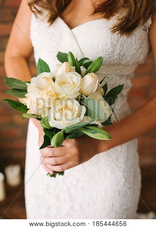 Bride in a white elegants lacy wedding dress holding a flowers bouquet from white fresh rose in hands. Wedding bridal bouquet close up. Tenderness, love, wedding, fashion - concept.