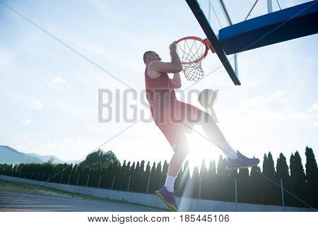 Young man jumping and making a fantastic slam dunk playing streetball, basketball. Urban authentic.