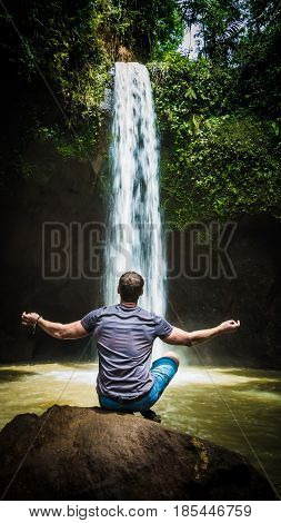 Man meditating in front of waterfall near Ubud, Bali, Indonesia.