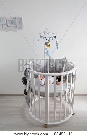 newborn lies in the round white bed with mobile and toys